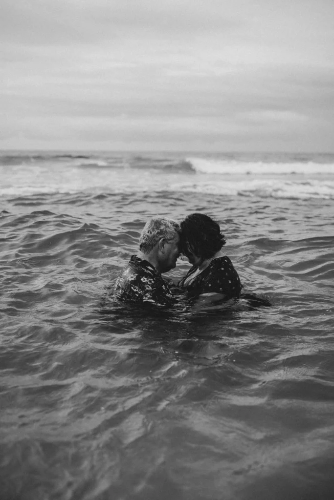 Couple enjoying a romantic photoshoot in the water, surrounded by soft waves and a serene atmosphere, capturing their love in a beautiful natural setting