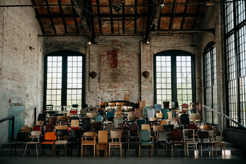 Rows of eclectic vintage chairs in front of exposed brick and tall windows