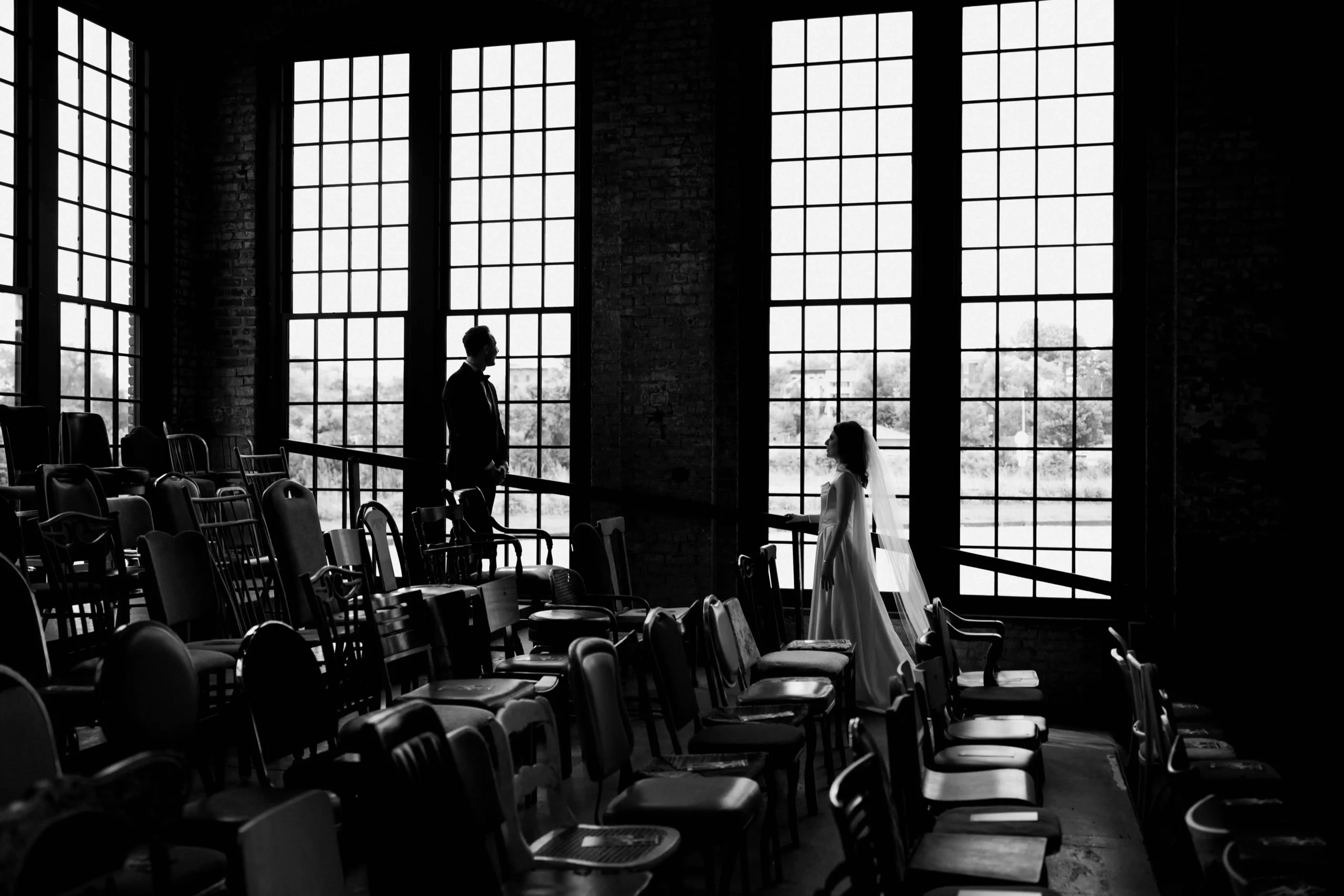 Bride and groom walking through a room full of vintage chairs in a loft-style venue