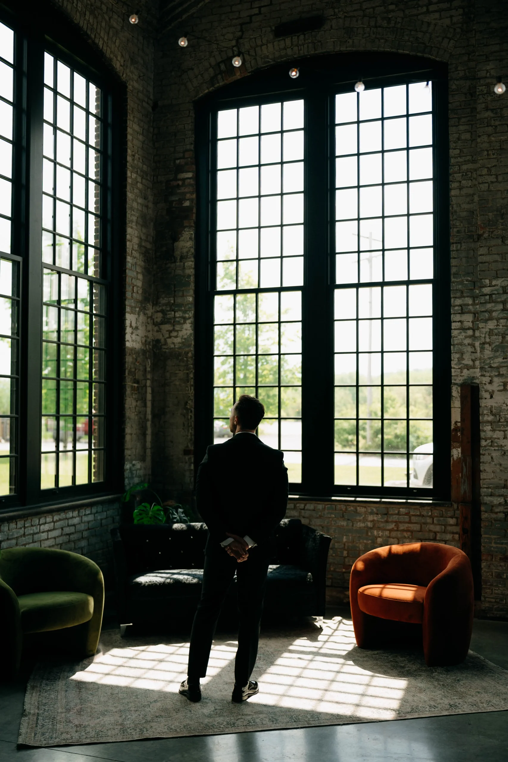 Groom waiting alone in a room with tall industrial windows.