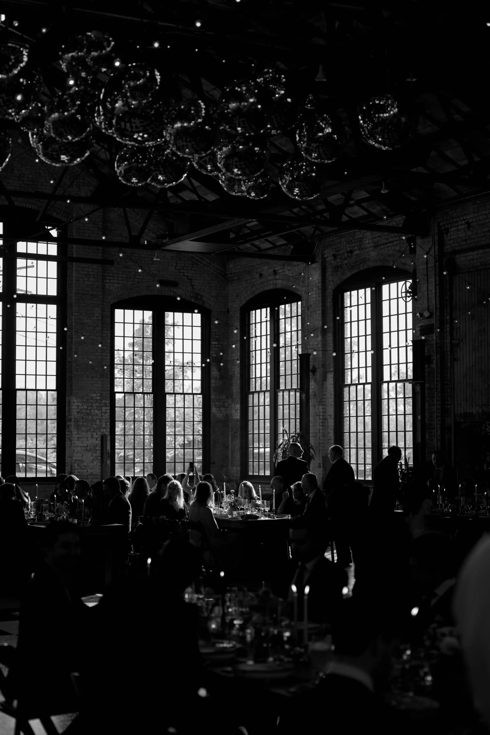 Black-and-white photo of wedding guests dining at Hudson Basilica with moody window light.