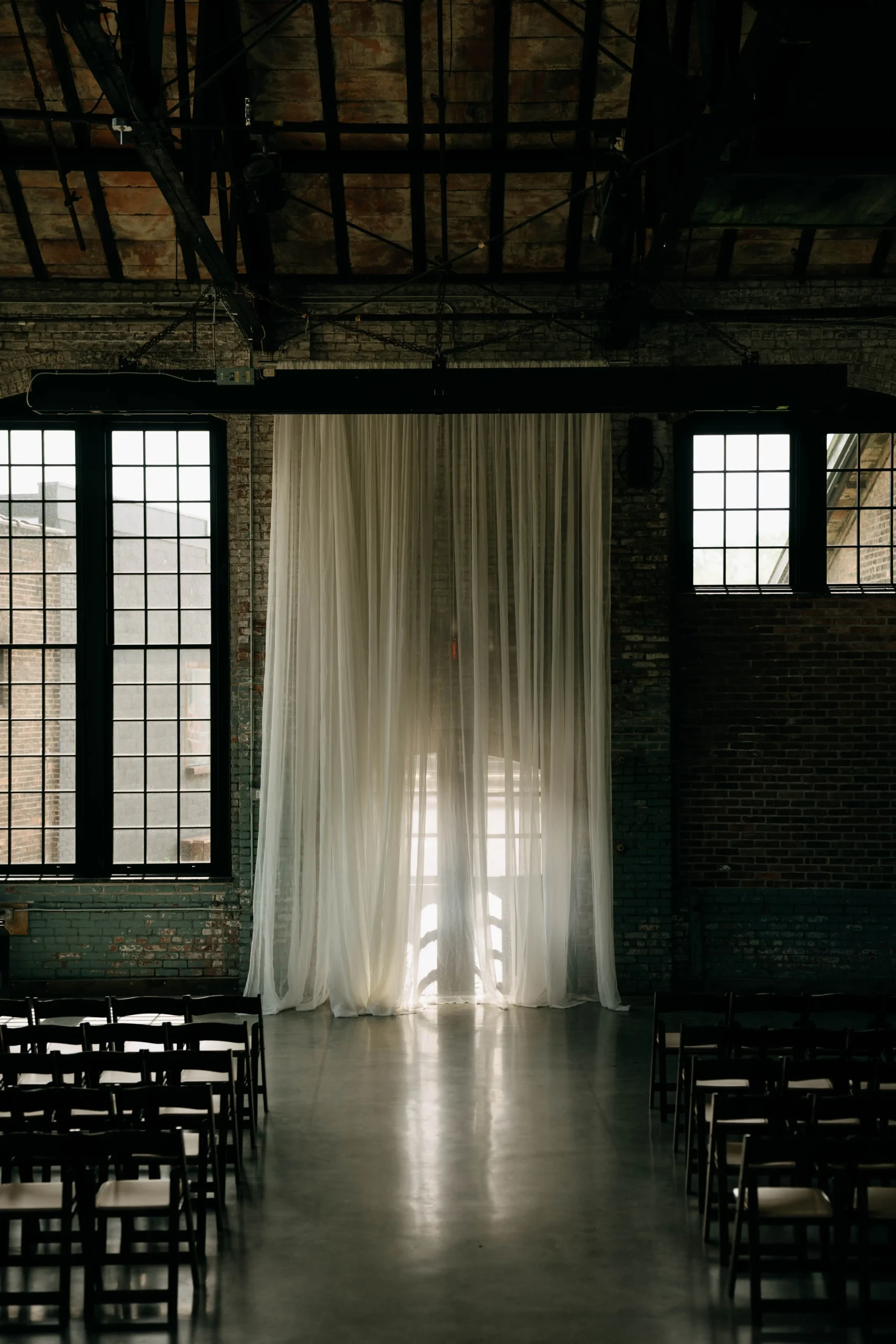 Ceremony setup inside Basilica Hudson with sheer curtains and moody natural light.