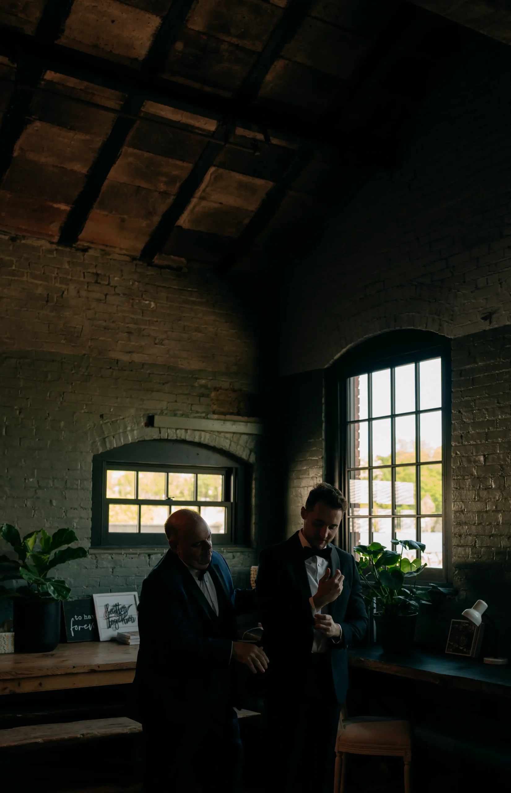 Tom adjusting his cufflinks with his father in a moody room.