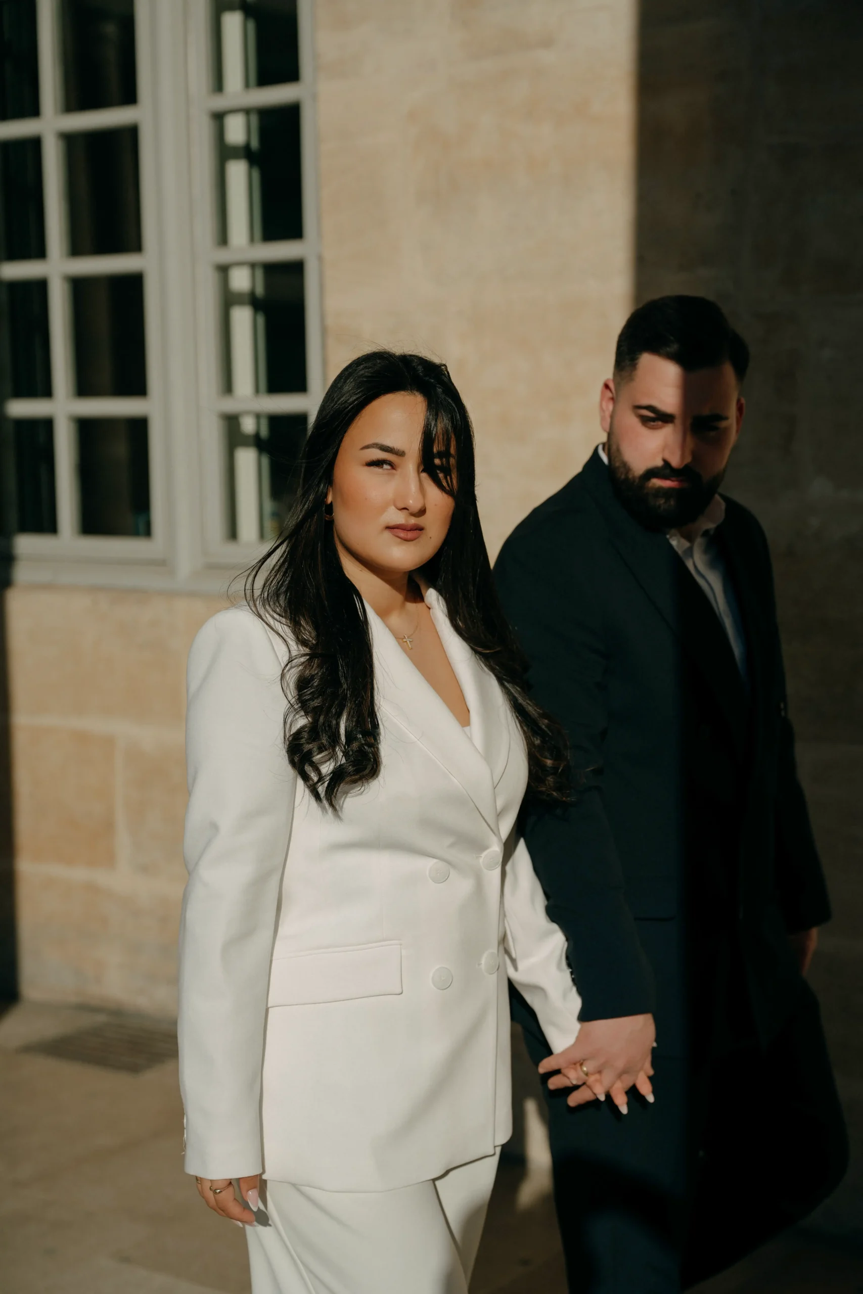 Bride and groom walking through sunlit Parisian columns.