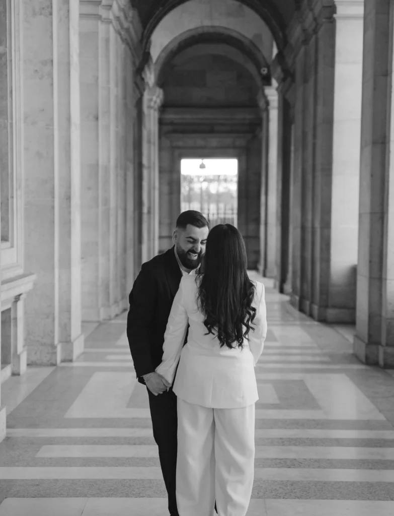 Couple walking hand in hand under classic arches in Paris.