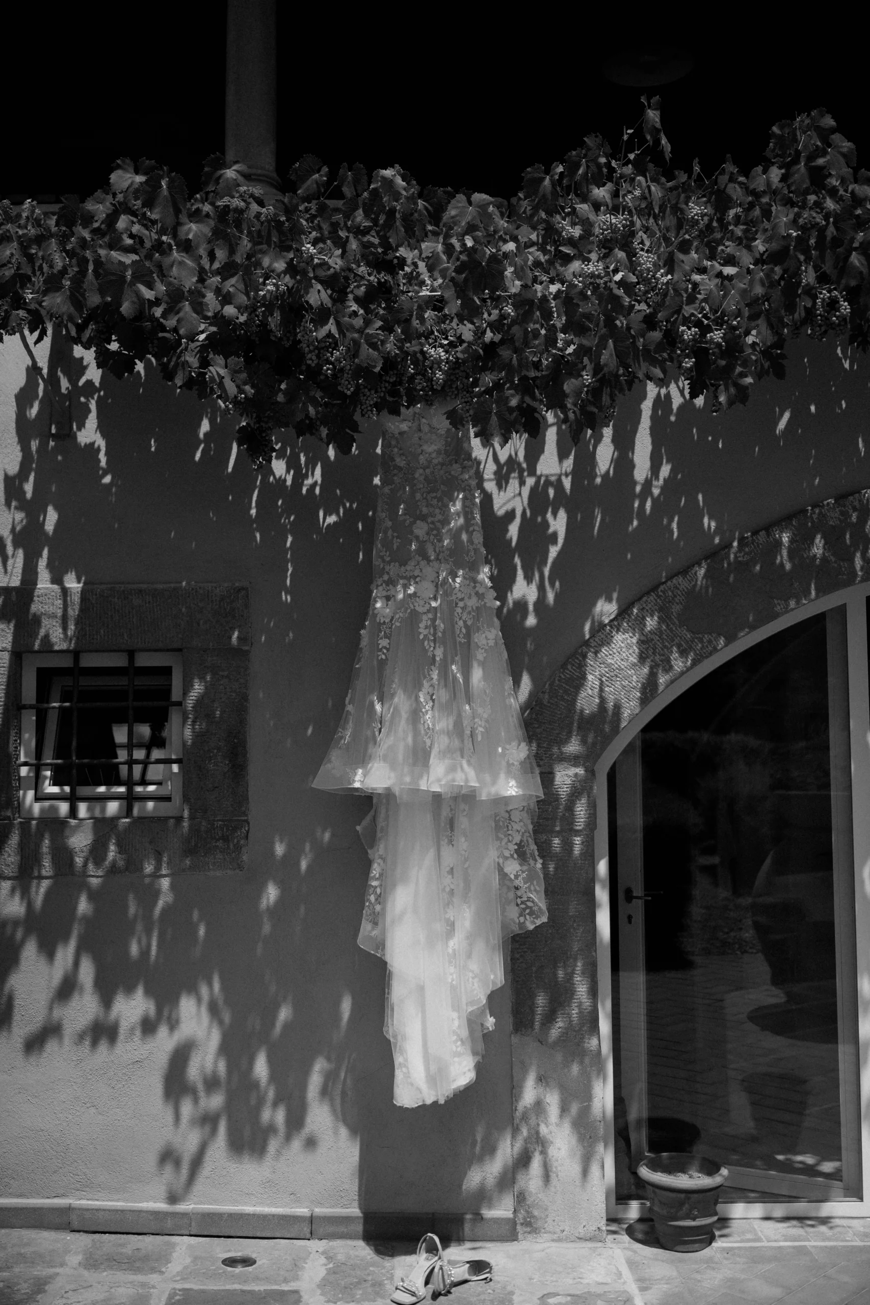 Wedding dress hanging in Tuscany courtyard – black and white detail with dramatic natural light and shadows