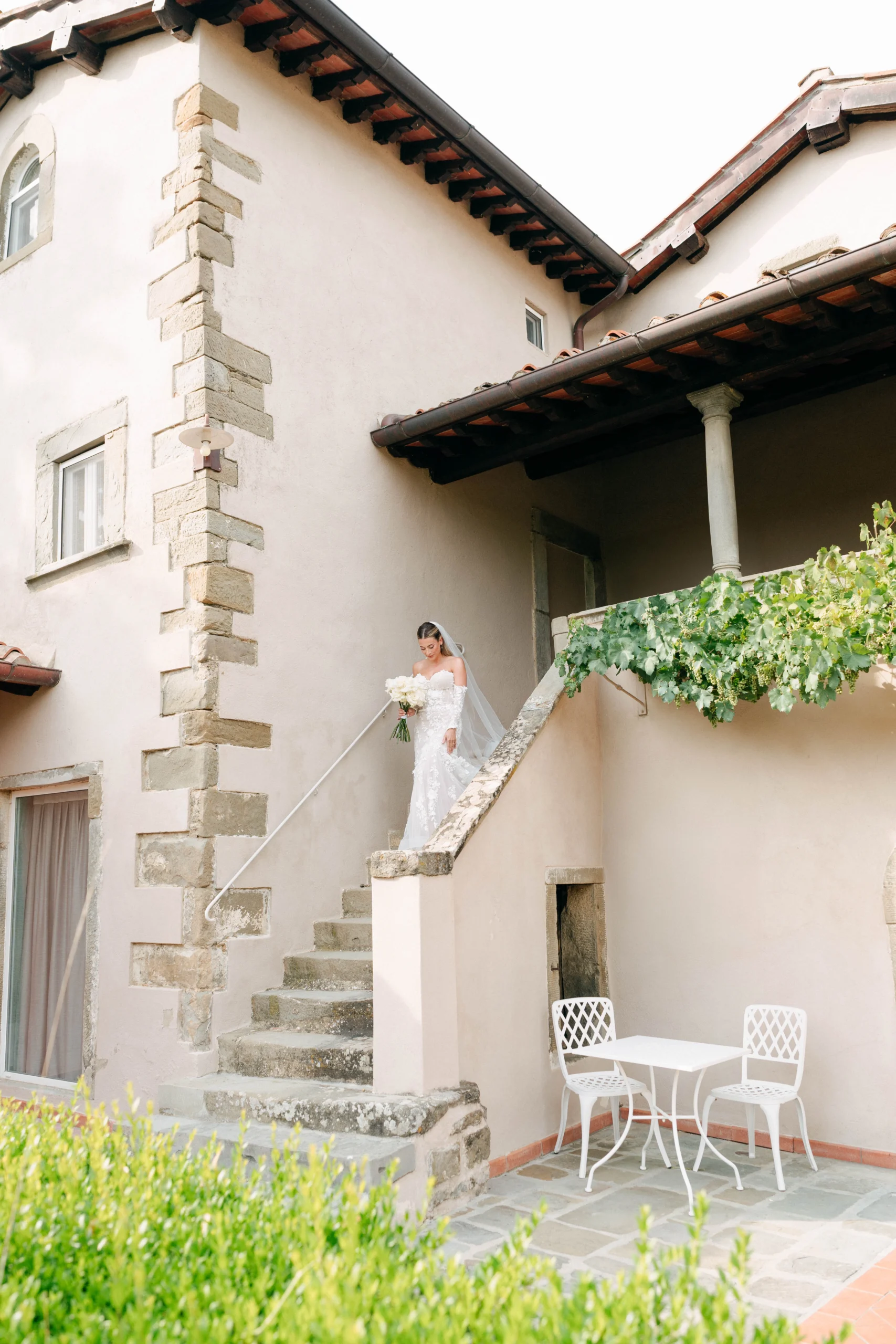A quiet and intimate getting ready moment as the groom receives help adjusting his collar, standing in front of a sunlit balcony with views of Tuscany’s countryside — cinematic and honest.