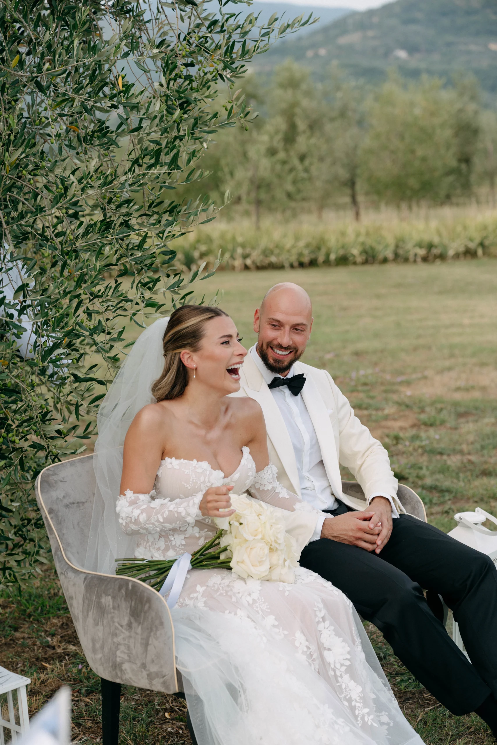 Bride and groom laughing together under an olive tree in Tuscany