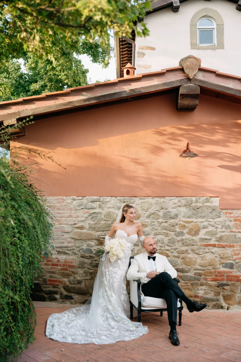 Bride laughing with bridesmaids as she puts on her wedding dress, capturing a moment of joy and excitement Wedding couple in Tuscany standing against a rustic wall – romantic and editorial destination wedding vibe