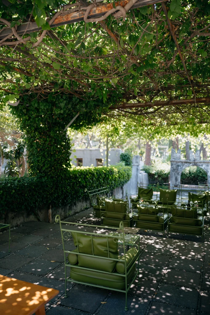 Schattige Terrasse unter einer Pergola mit Efeu und grünen Vintage-Stühlen auf Sizilien