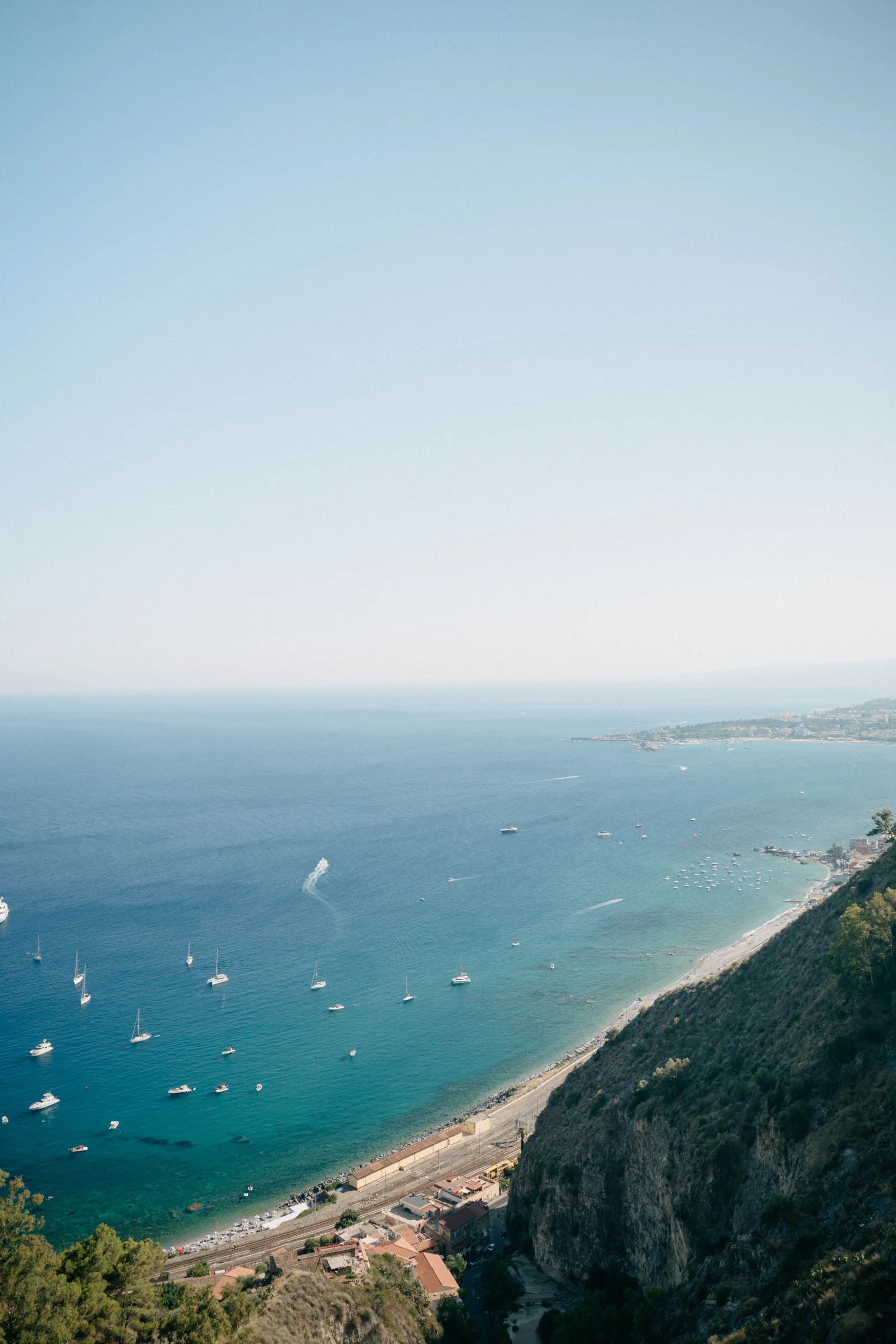 Aerial view of the Sicilian coastline with turquoise waters and boats near Taormina.