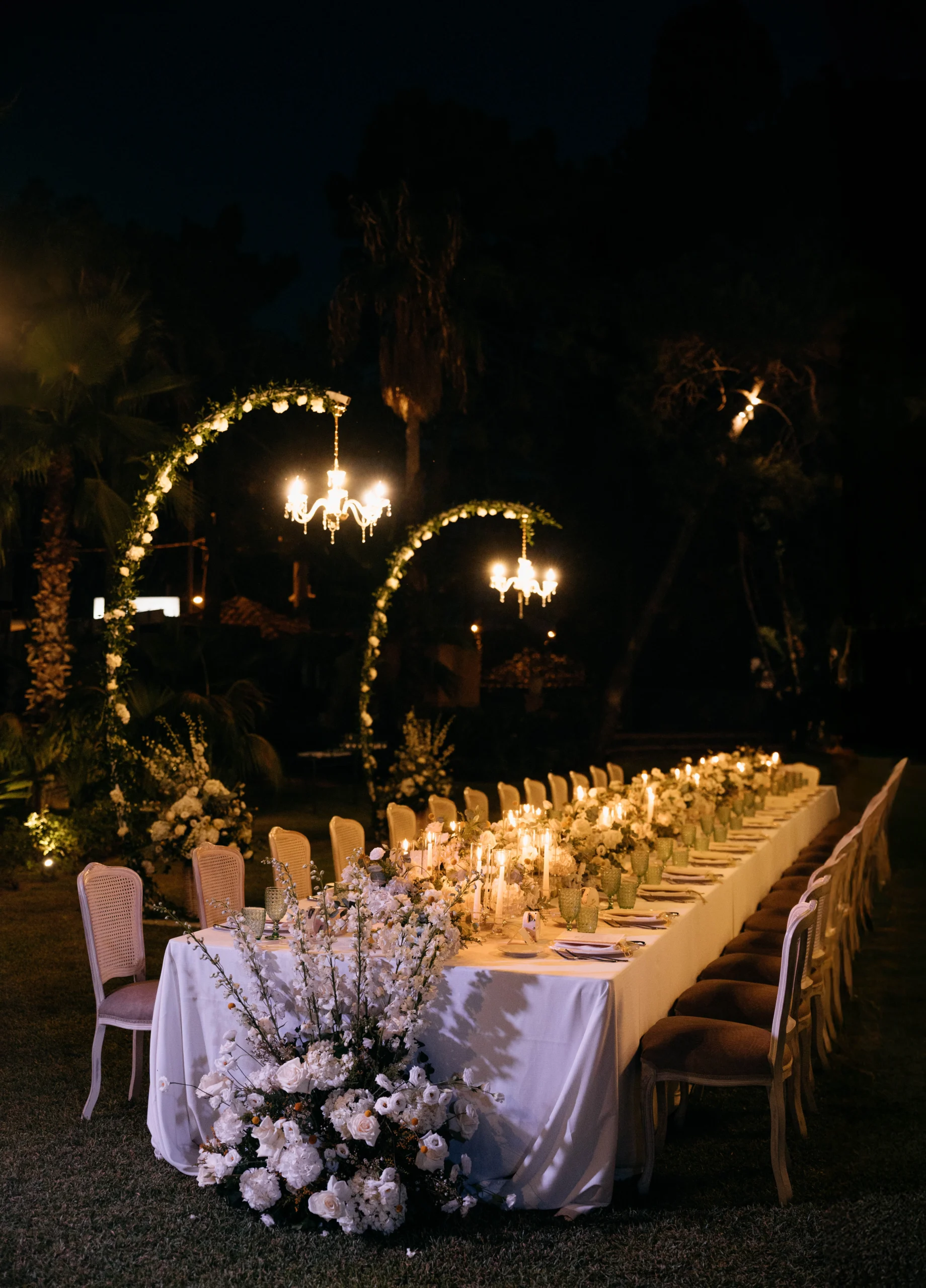 Elegant long wedding dinner table with candlelight and floral decor under chandeliers.