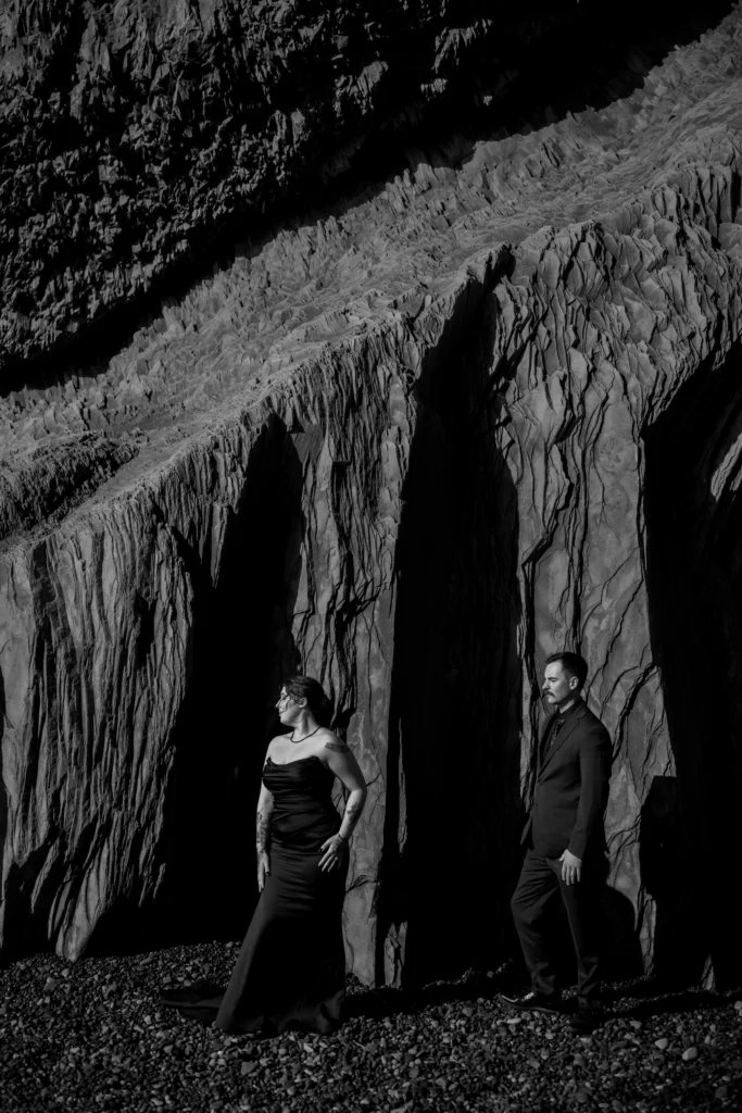 Black-and-white photo of couple standing in tall rock crevices on beach