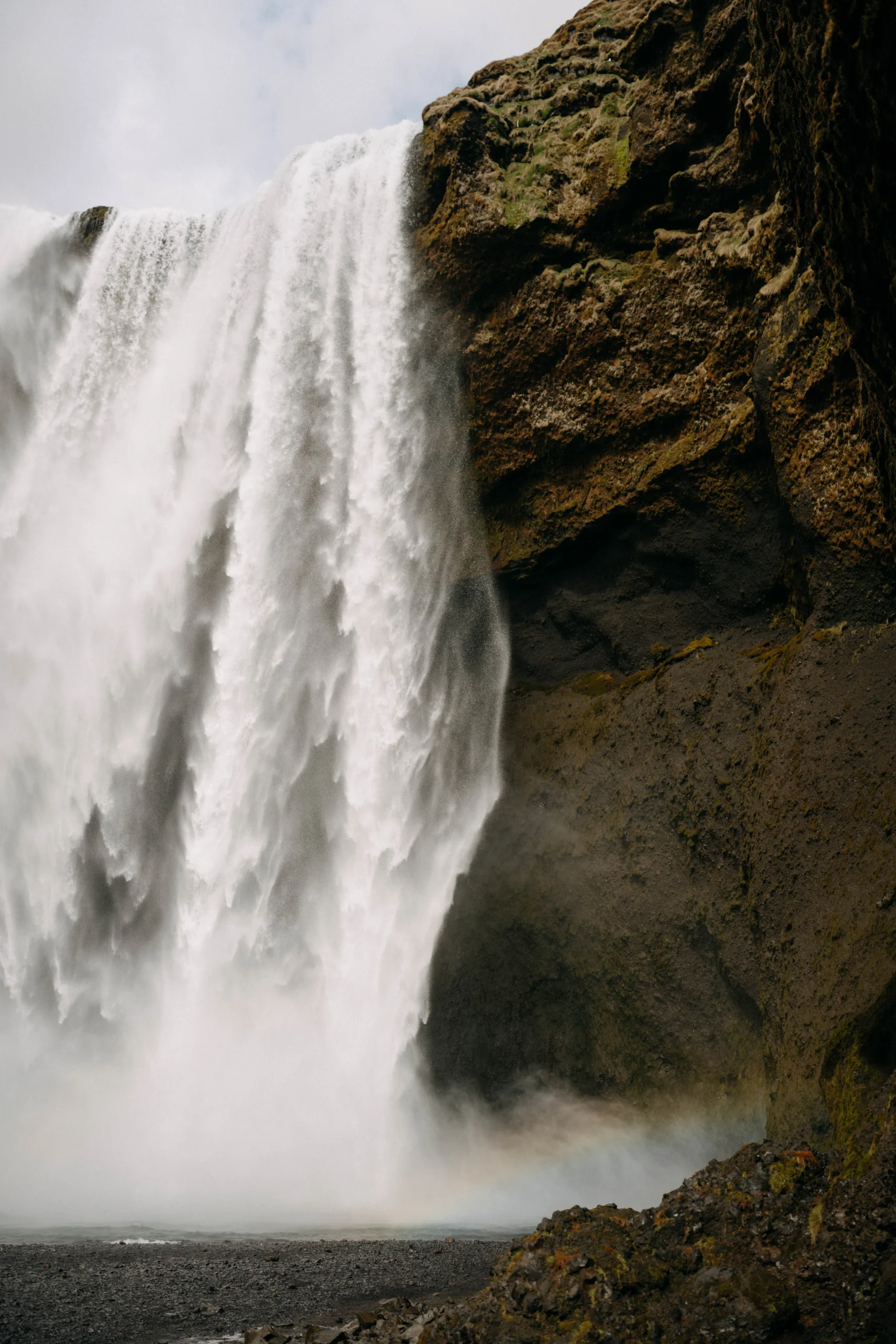 Massive waterfall cascading over black cliffs in Iceland, mist rising at the base.