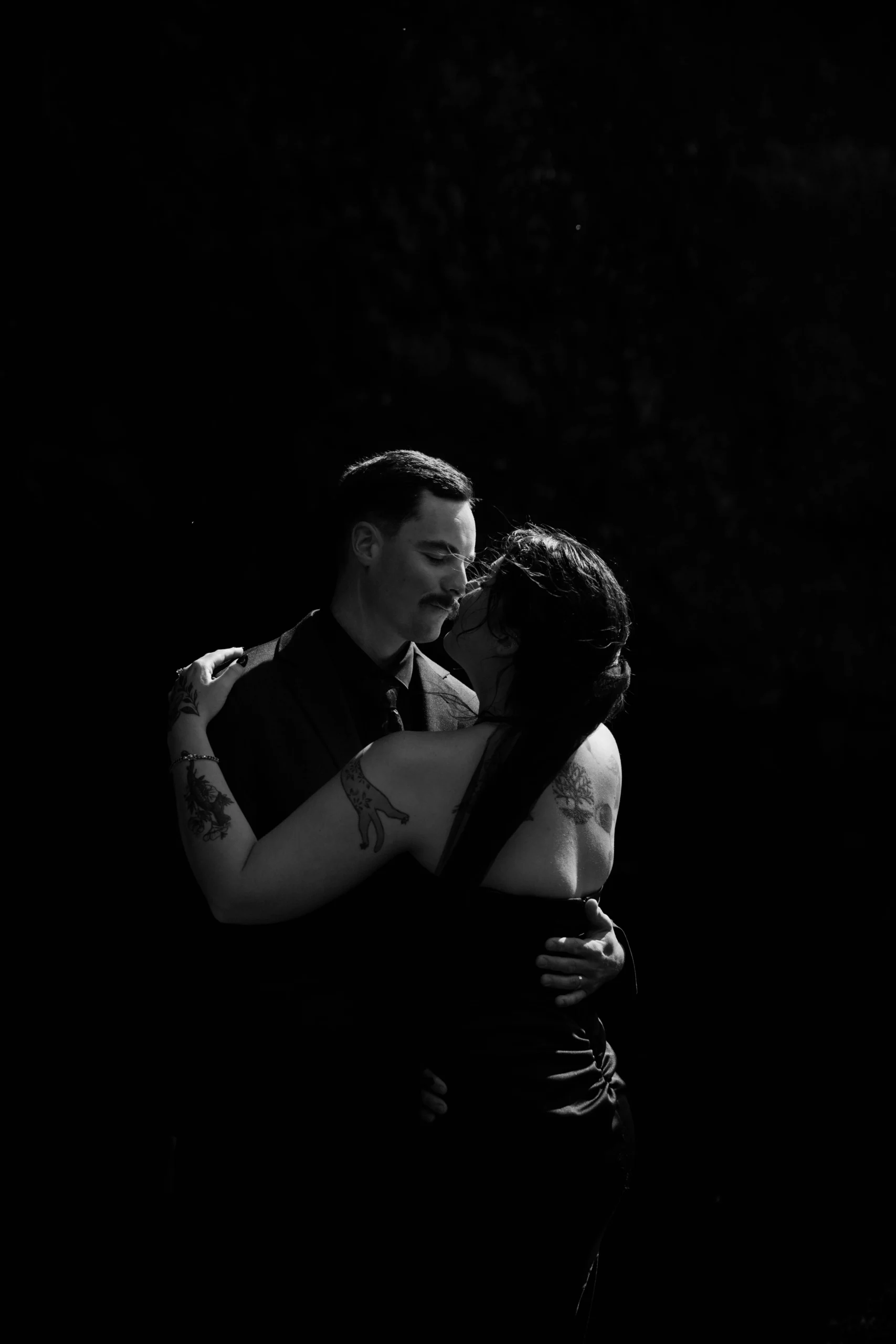 Black-and-white close-up of couple in tight embrace with visible tattoos