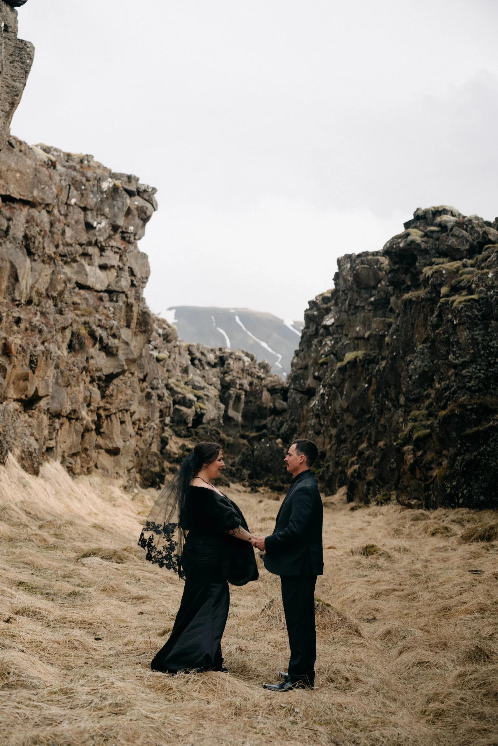 Couple holding hands in Icelandic rock canyon, bride wearing lace veil