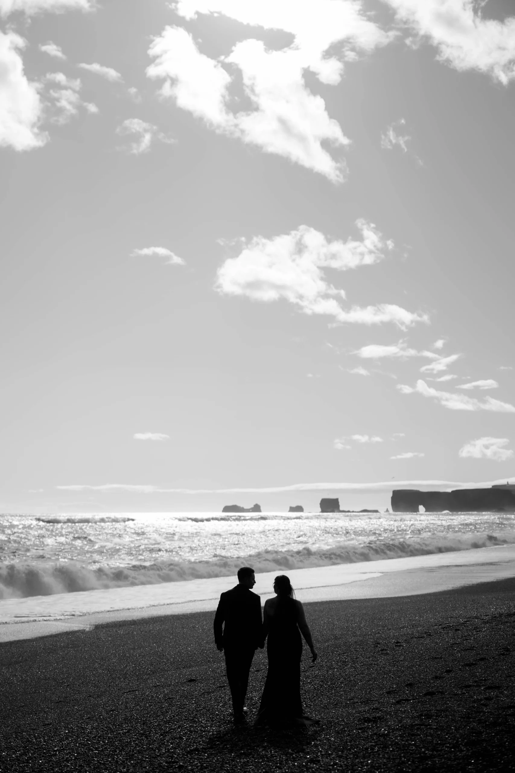 Black-and-white silhouette of couple on black sand beach with waves