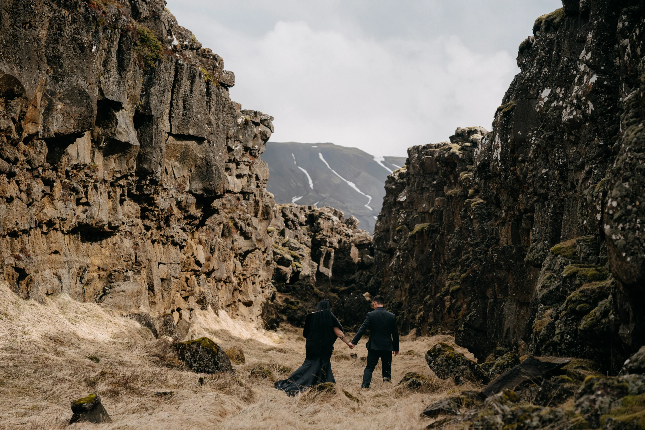 Couple walking hand in hand through Icelandic rock canyon with mountain view