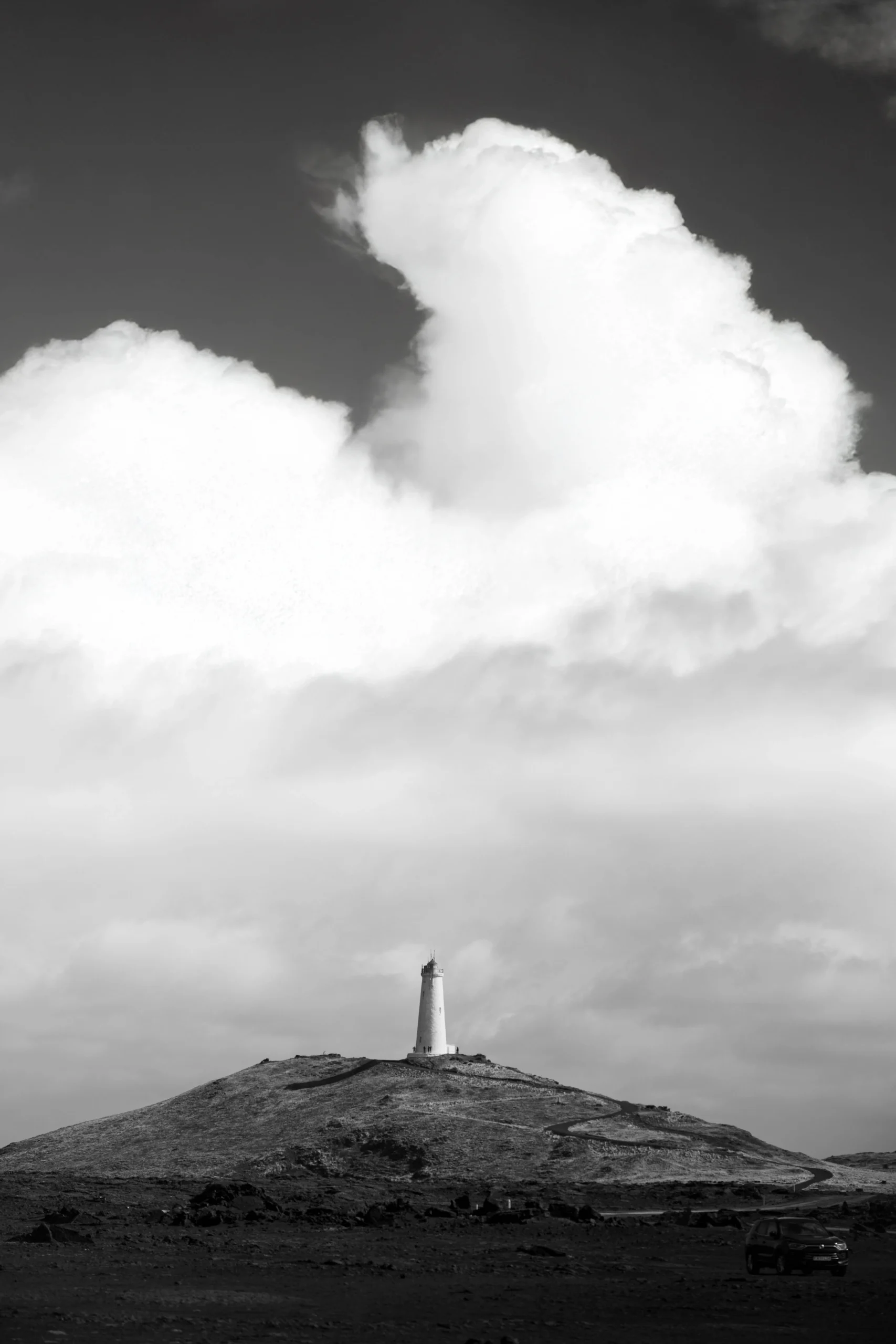 White lighthouse on grassy hill under cloudy sky, Iceland