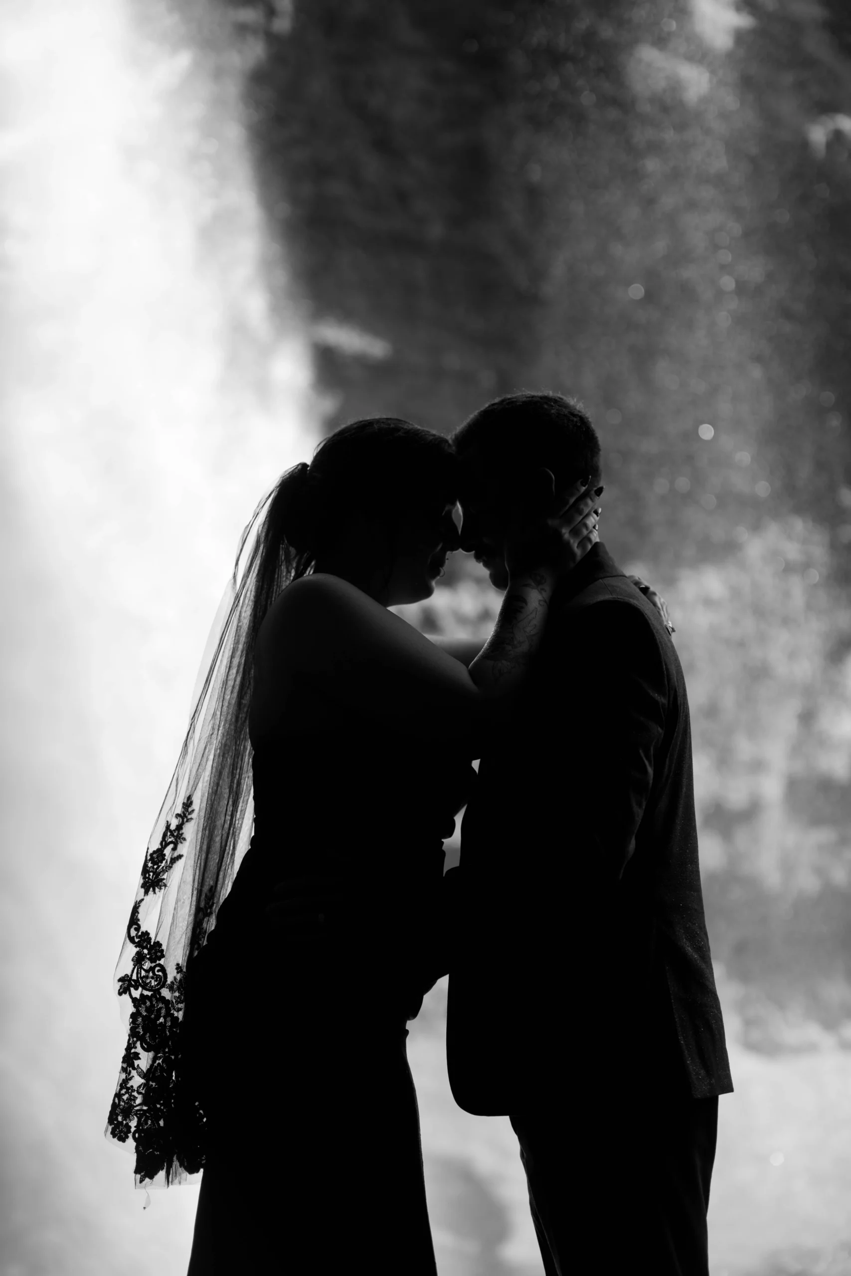 Black-and-white silhouette of couple forehead to forehead in front of waterfall