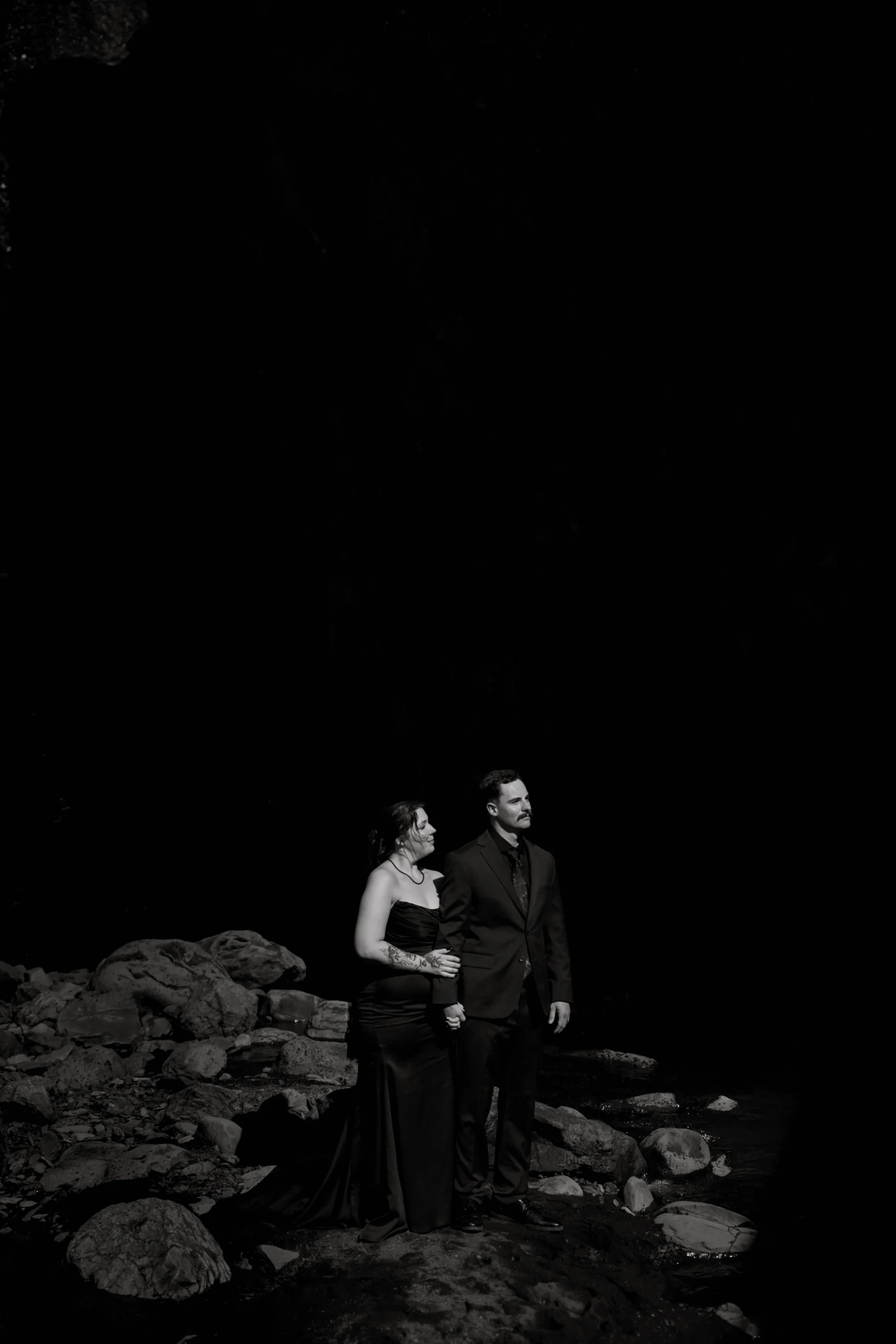 Silhouette of couple on rocks by the water, dramatic black and white