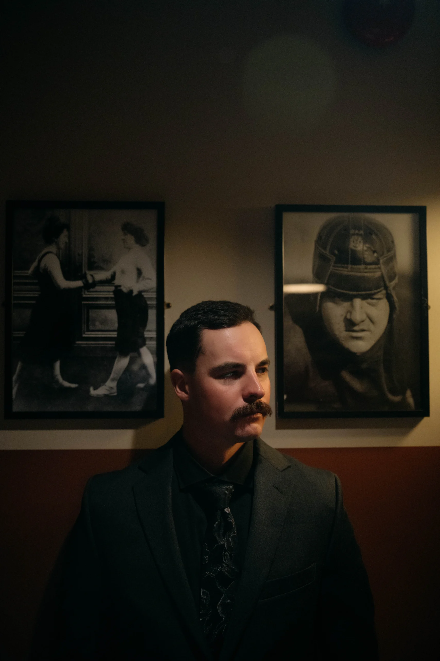 Groom with mustache standing before historic boxing photos on the wall