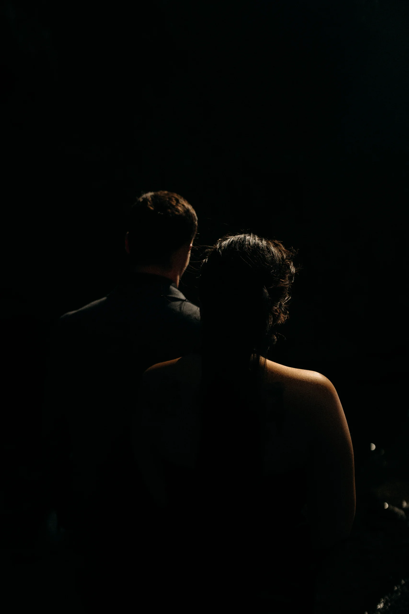 Silhouette of couple from behind in dark room, intimate embrace